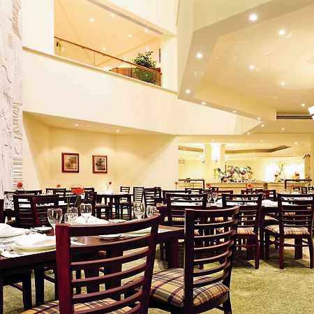 Movenpick Taba Resort & Spa Eksteriør billede The photo shows the interior of a restaurant. The space features several tables arranged with chairs, and there's a cozy ambiance created by soft lighting. The walls are designed with a decorative element, possibly a relief, and there are some framed