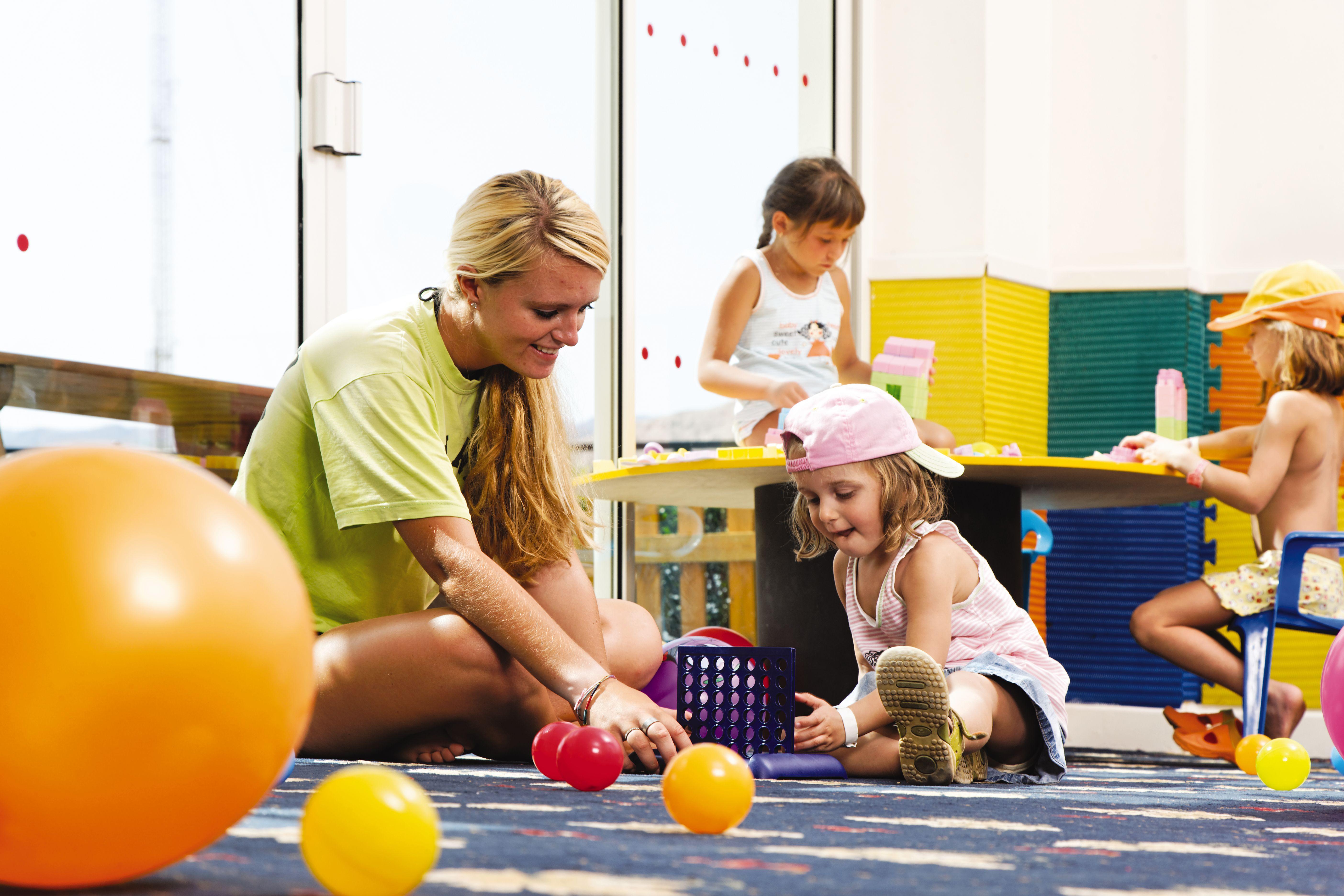 Movenpick Taba Resort & Spa Eksteriør billede The photo shows a playful and colorful indoor environment, likely a playroom or daycare. In the foreground, a young woman is sitting on the floor with a young girl, engaging in play with various colorful balls. The girl is wearing a pink cap and appe