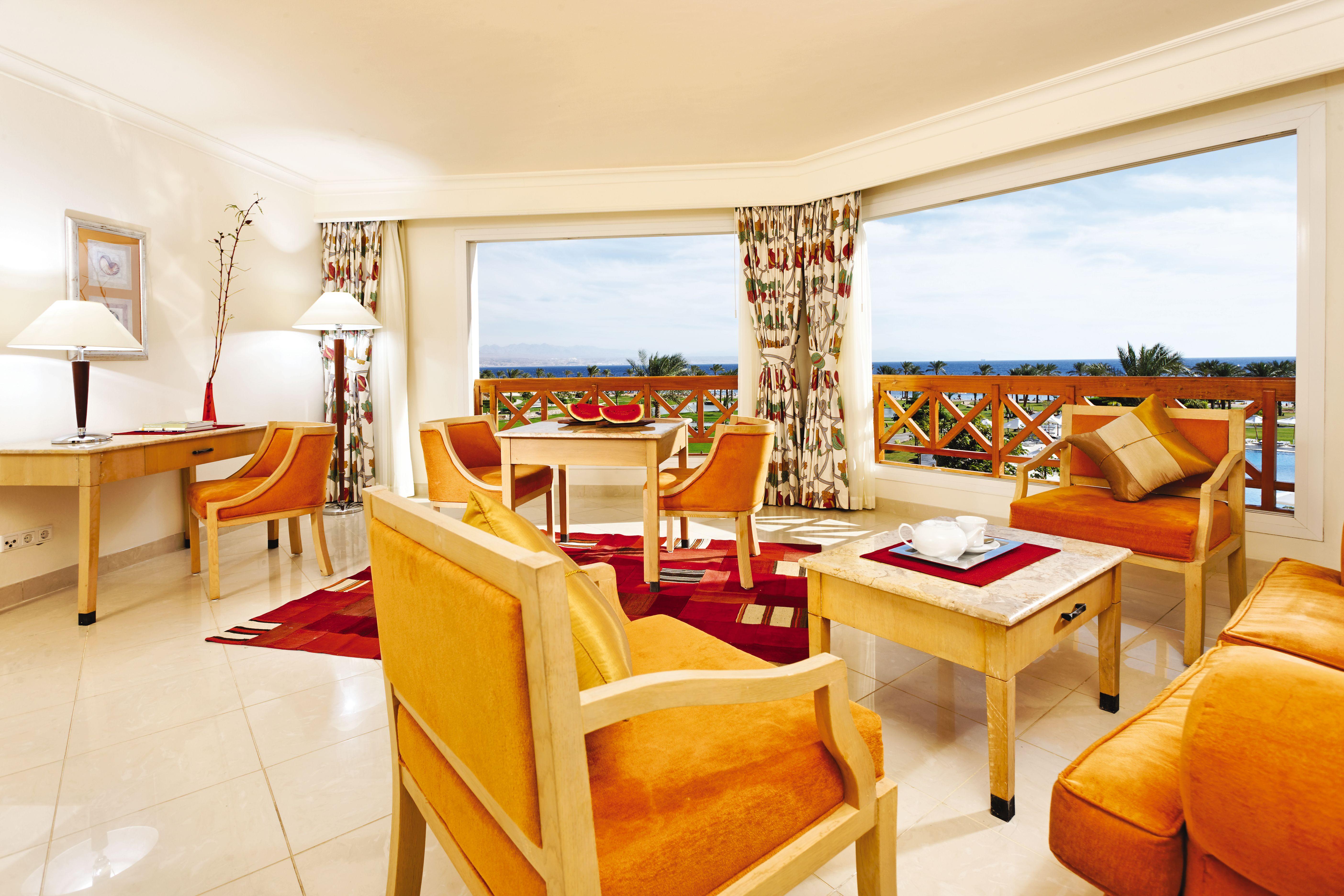 Movenpick Taba Resort & Spa Eksteriør billede The photo shows a bright and upscale hotel suite. It features a spacious living area with large windows that offer a scenic view outside. The decor includes warm-toned furniture, such as orange armchairs and wooden tables. There is a small dining tab