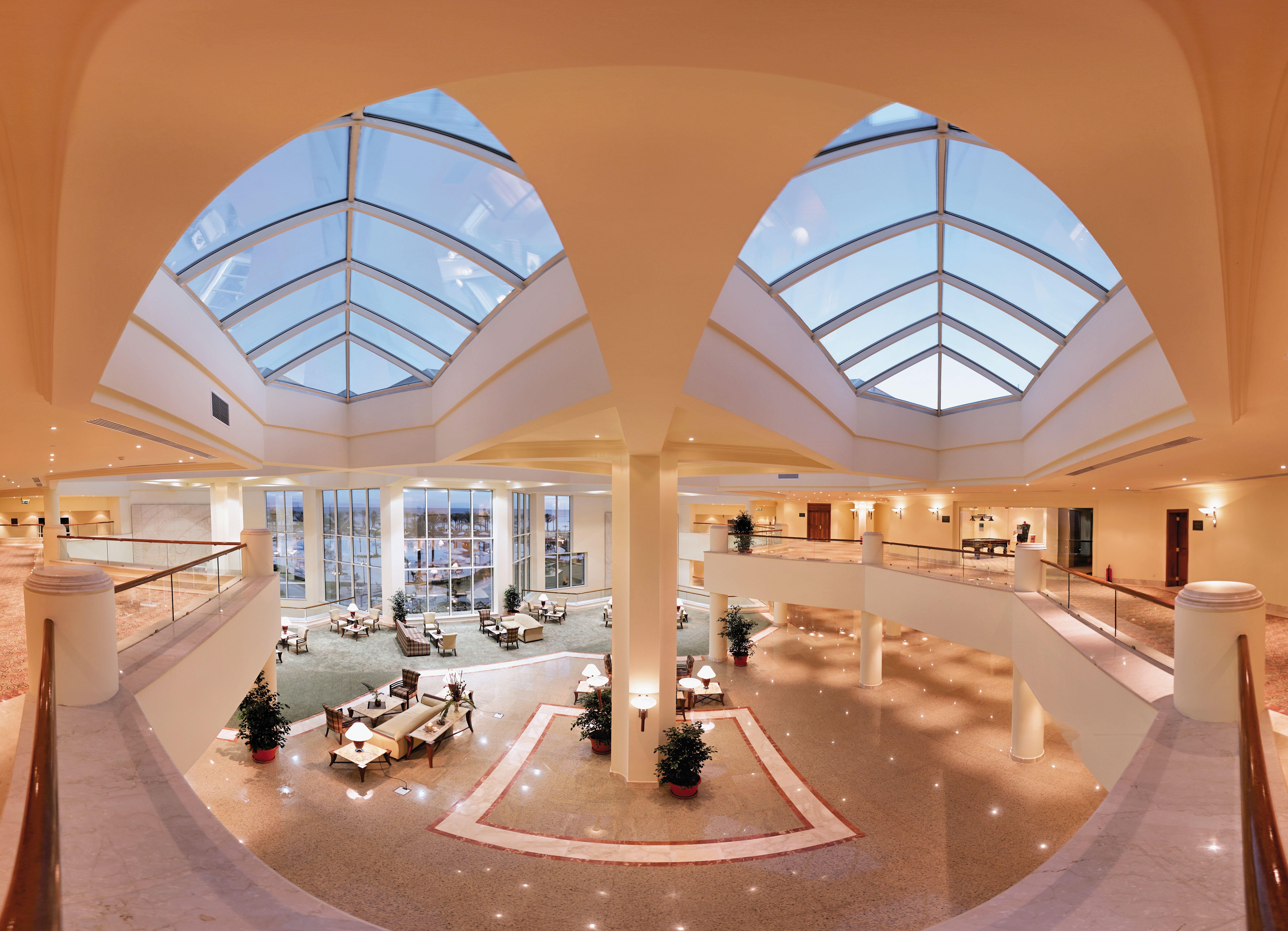 Movenpick Taba Resort & Spa Eksteriør billede The photo shows an elegant and spacious lobby area of a building, likely a hotel or a large public space. The interior features high ceilings with large skylights that allow natural light to flood the area. There are several seating arrangements, inc