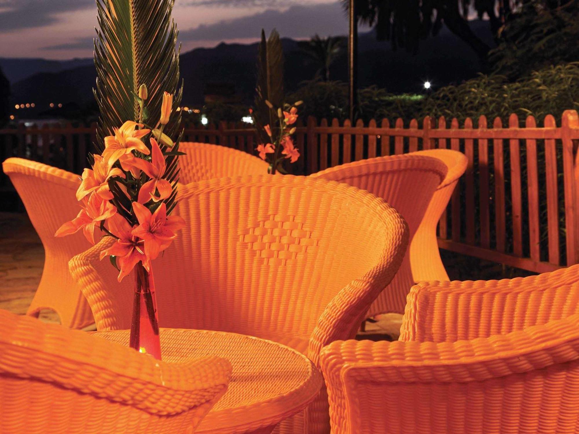 Movenpick Taba Resort & Spa Eksteriør billede The photo shows a cozy outdoor setting with a round table surrounded by several wicker chairs. Each chair has a unique, curvy design and is bathed in warm, soft lighting, creating an inviting atmosphere. In the center of the table, there is a decorat
