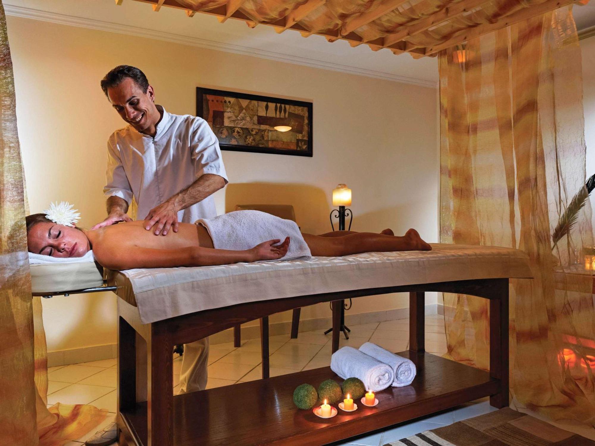 Movenpick Taba Resort & Spa Eksteriør billede The image depicts a serene spa setting where a therapist is giving a massage to a client lying on a massage table. The client is covered with a towel and has a flower in her hair, suggesting a relaxing and tranquil atmosphere. The room is softly lit 