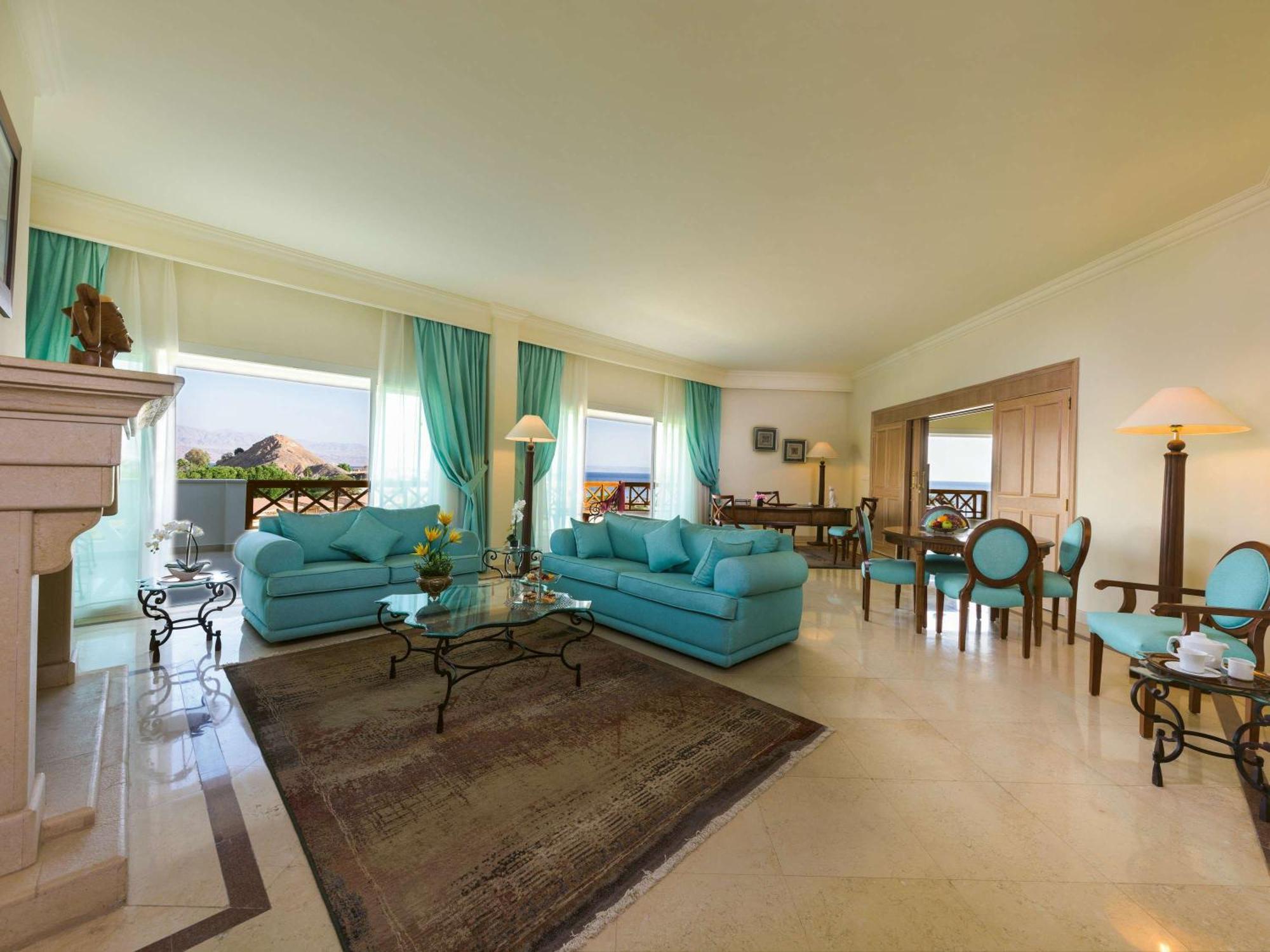 Movenpick Taba Resort & Spa Eksteriør billede The photo shows a spacious and elegantly designed living area. It features two light blue sofas arranged around a glass coffee table, creating a cozy seating area. There are large windows dressed with sheer curtains, allowing natural light to fill th