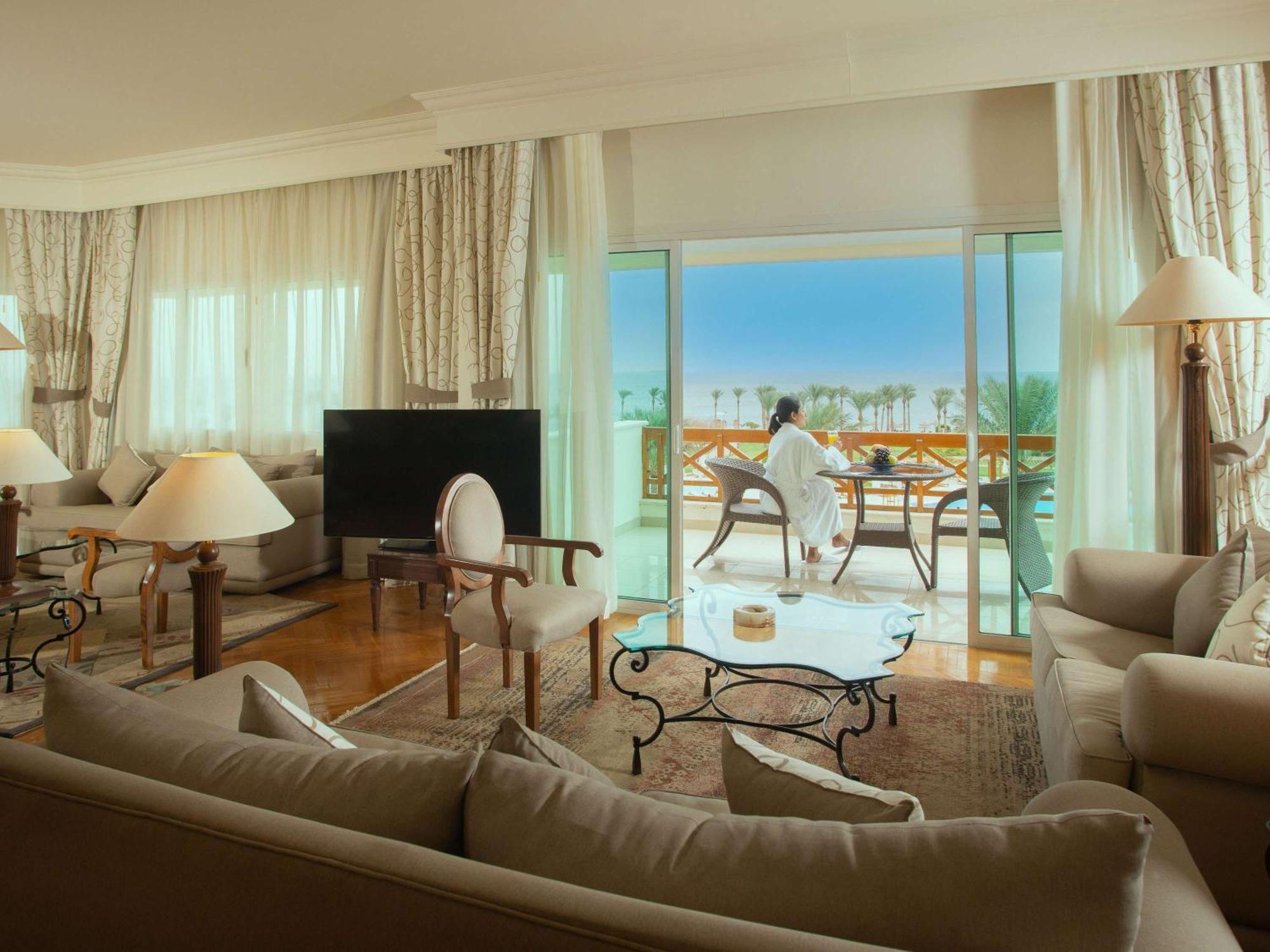 Movenpick Taba Resort & Spa Eksteriør billede The photo depicts a luxurious hotel suite. Inside, there is a spacious living area with elegant furnishings, including a large sofa, stylish armchairs, and a glass coffee table. A flat-screen TV is positioned in one corner. The large windows allow na